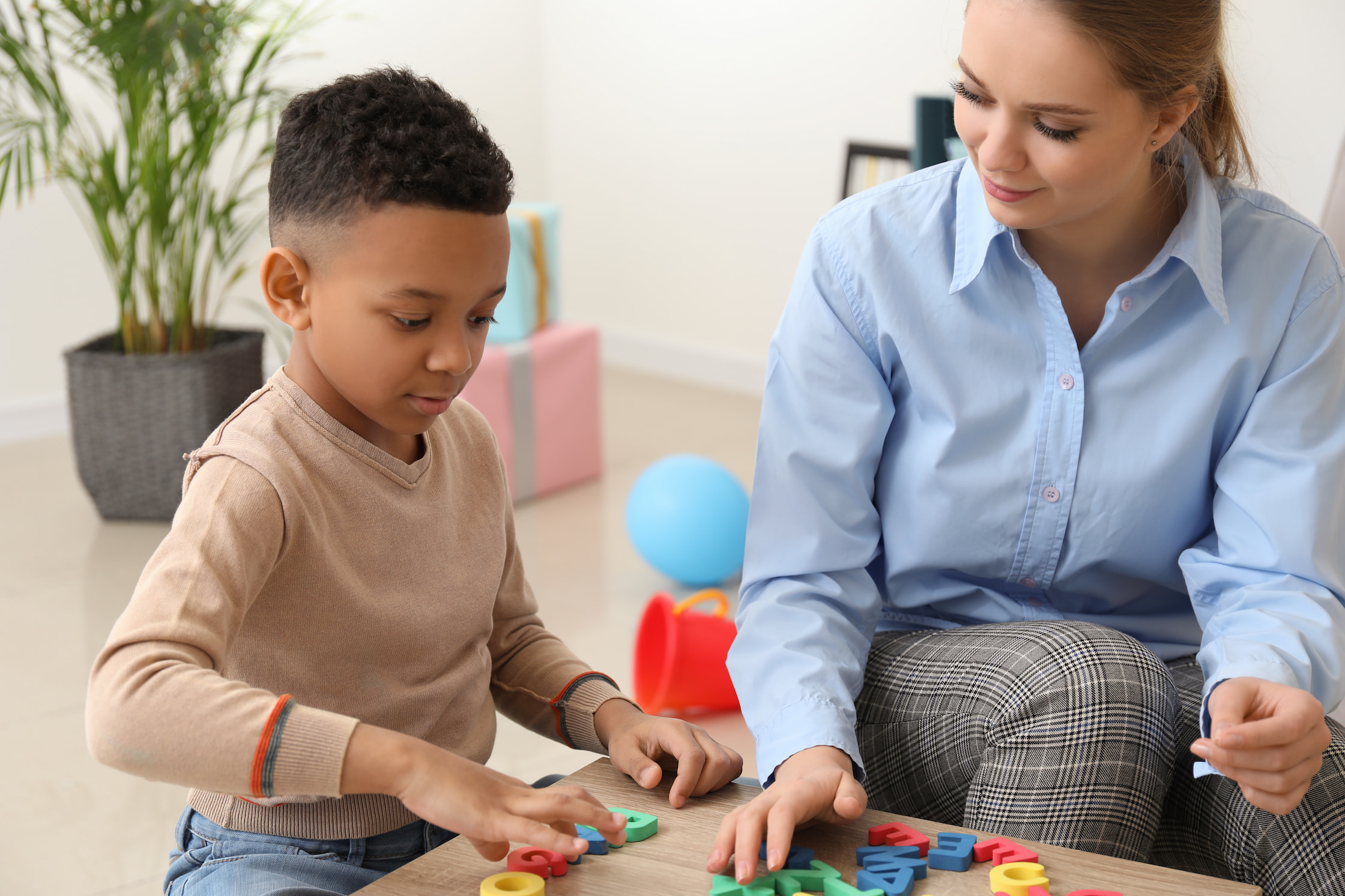 Enfant avec une orthophoniste composant des mots avec des lettres sur un bureau.