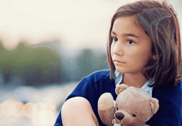 Enfant pensive tenant un ourson en peluche, illustrant les effets des difficultés langagières sur la confiance en soi.