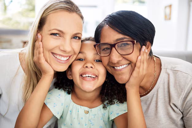 Enfant souriante entourée de deux adultes qui la tiennent par les joues, illustrant une famille chaleureuse et un environnement soutenant le développement du langage.