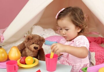 Petite fille qui joue à faire semblant en servant un repas à des toutous, illustrant le jeu symbolique.