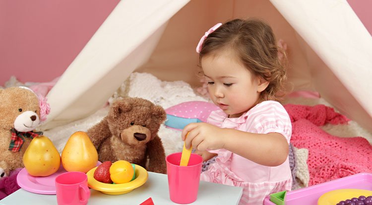 Petite fille qui joue à faire semblant en servant un repas à des toutous, illustrant le jeu symbolique.